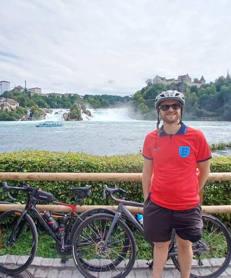 A photo of Ed Watson aka Eddy Explore in front of Rhine Falls in Germany with two bicycles.